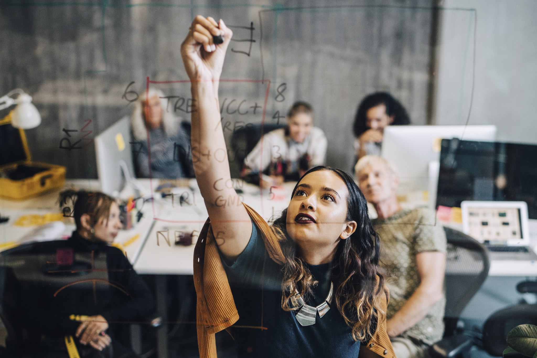 Businesswoman explaining strategy to colleagues while writing on glass Businesswoman explaining strategy to colleagues while writing on glass at IT company