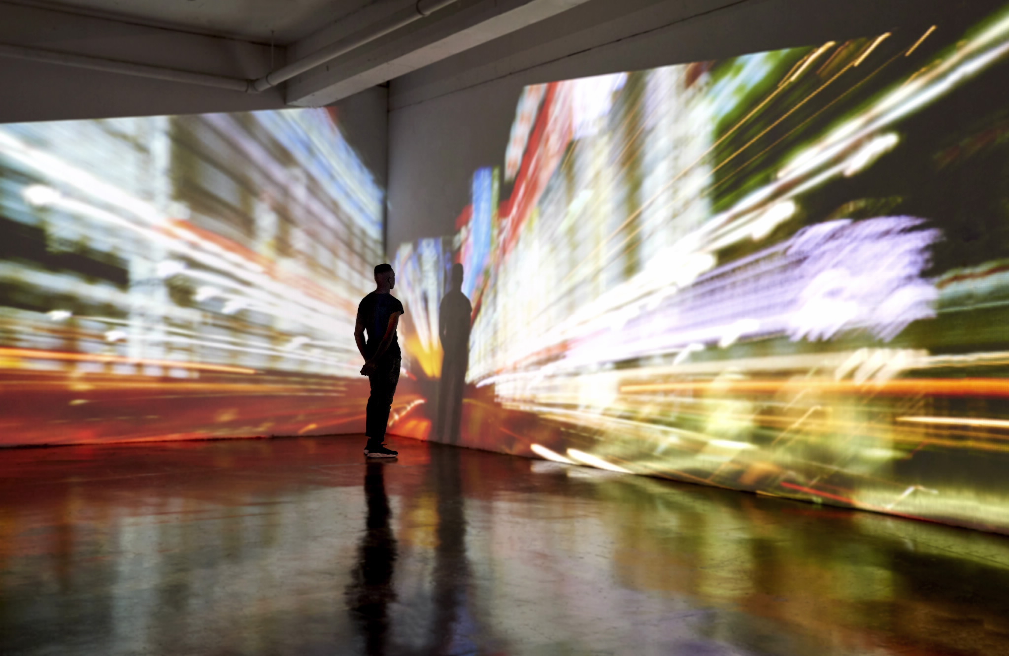 Person standing in a corner looking at an artistic light exhibit