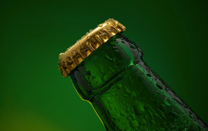 Extreme close-up of green bottle with water drops and golden cap on green background.