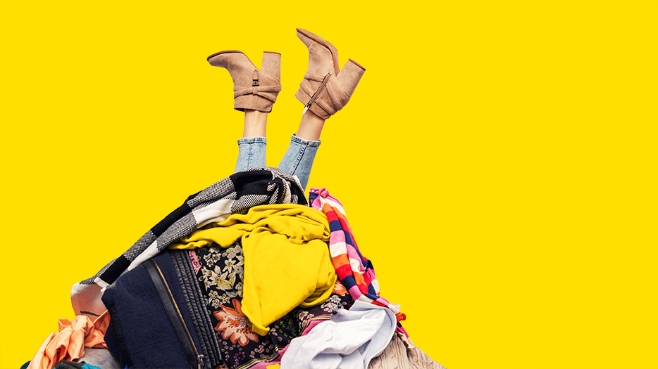 woman with legs out of clothes pile on yellow background