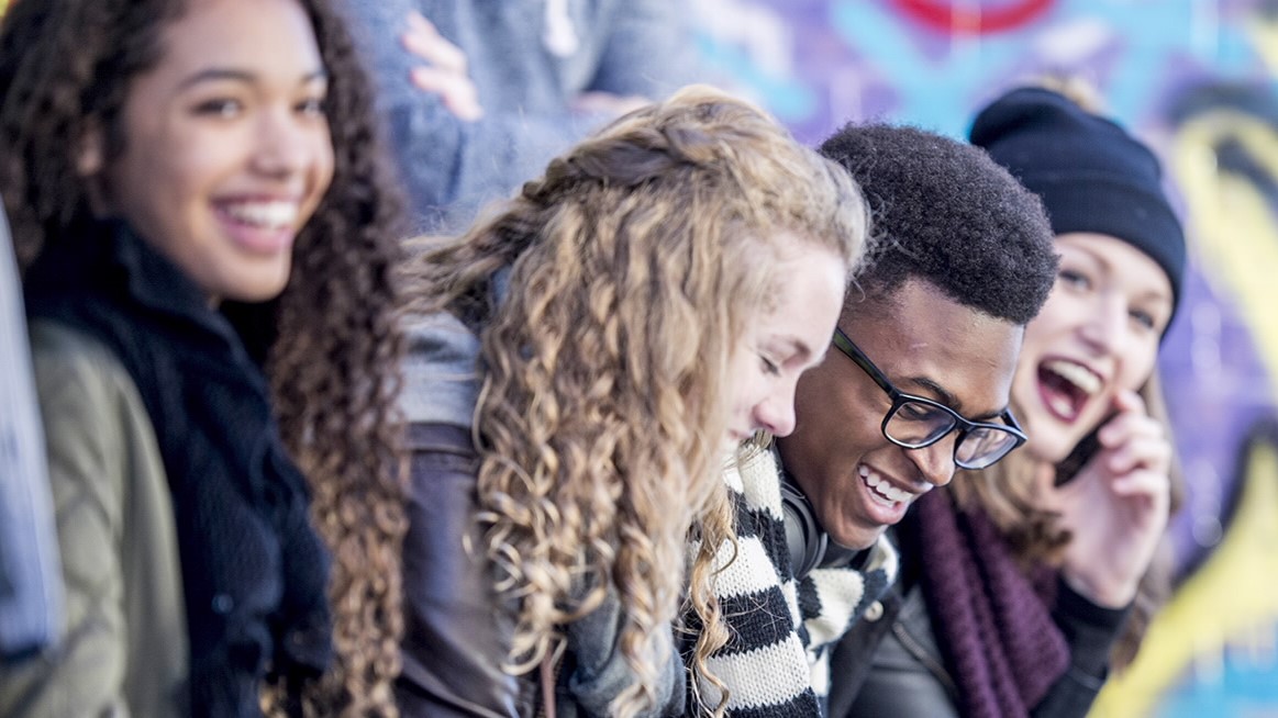 teenagers are sitting in front of a wall covered in graffiti