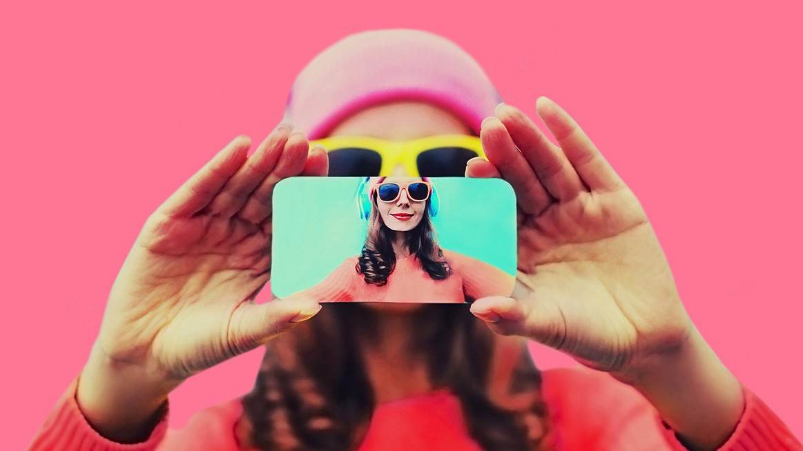 Close up of person stretching hands to take selfie with phone on pink background