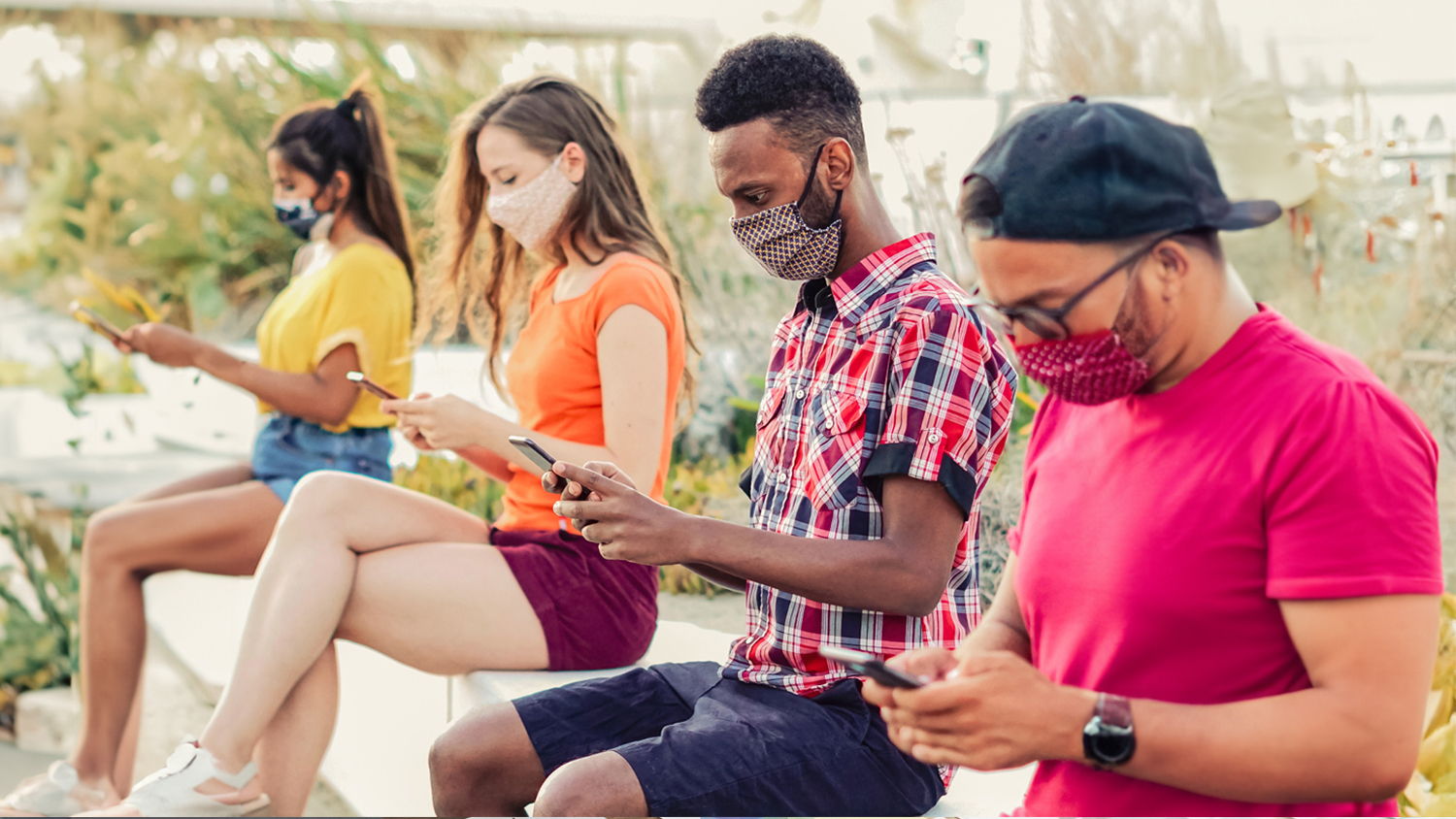 people sitting in a row with masks on texting