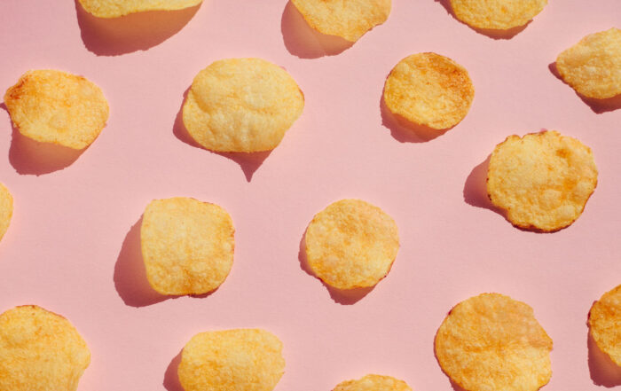 Potato chips pattern over pink background, hard light with shadows. Unhealthy junk food concept.