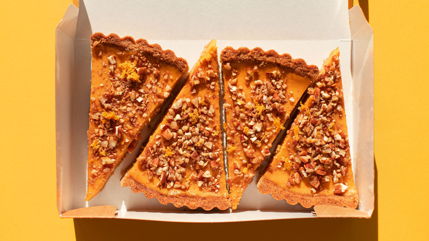 Four pieces of pumpkin cake with walnuts in a cardboard box on a orange table. A traditional autumn dish for Thanksgiving day and Halloween. Flat lay style