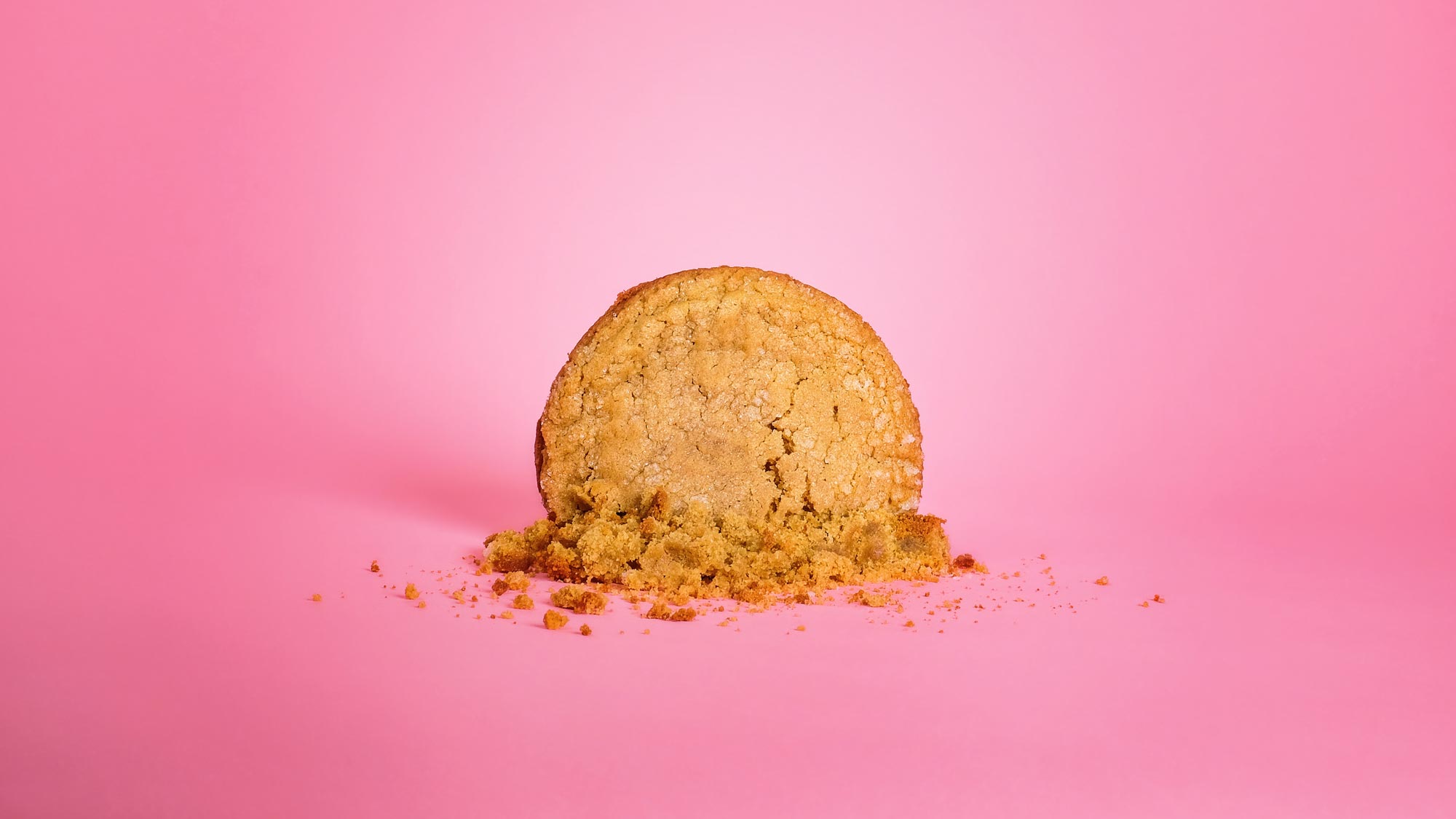 Large smashed homemade vegan, gluten free peanut butter cookie on a pink background