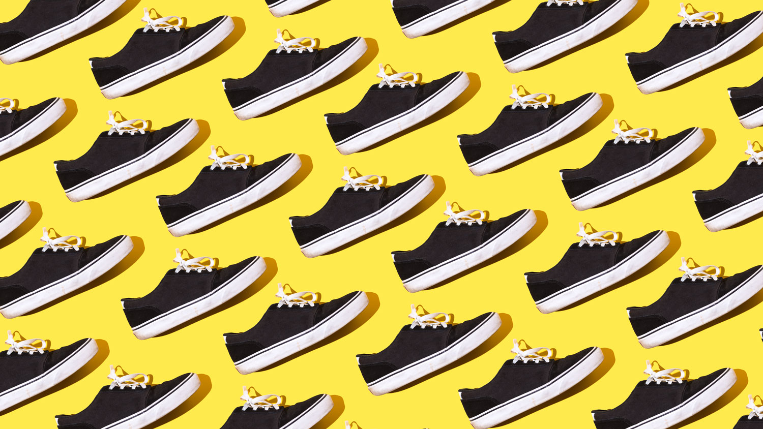Pattern of black and white canvas and rubber surfer and skater sneakers with white laces, on a yellow background. Concept of skateboarding, surfing, fashion, sneakers, modern and retro.