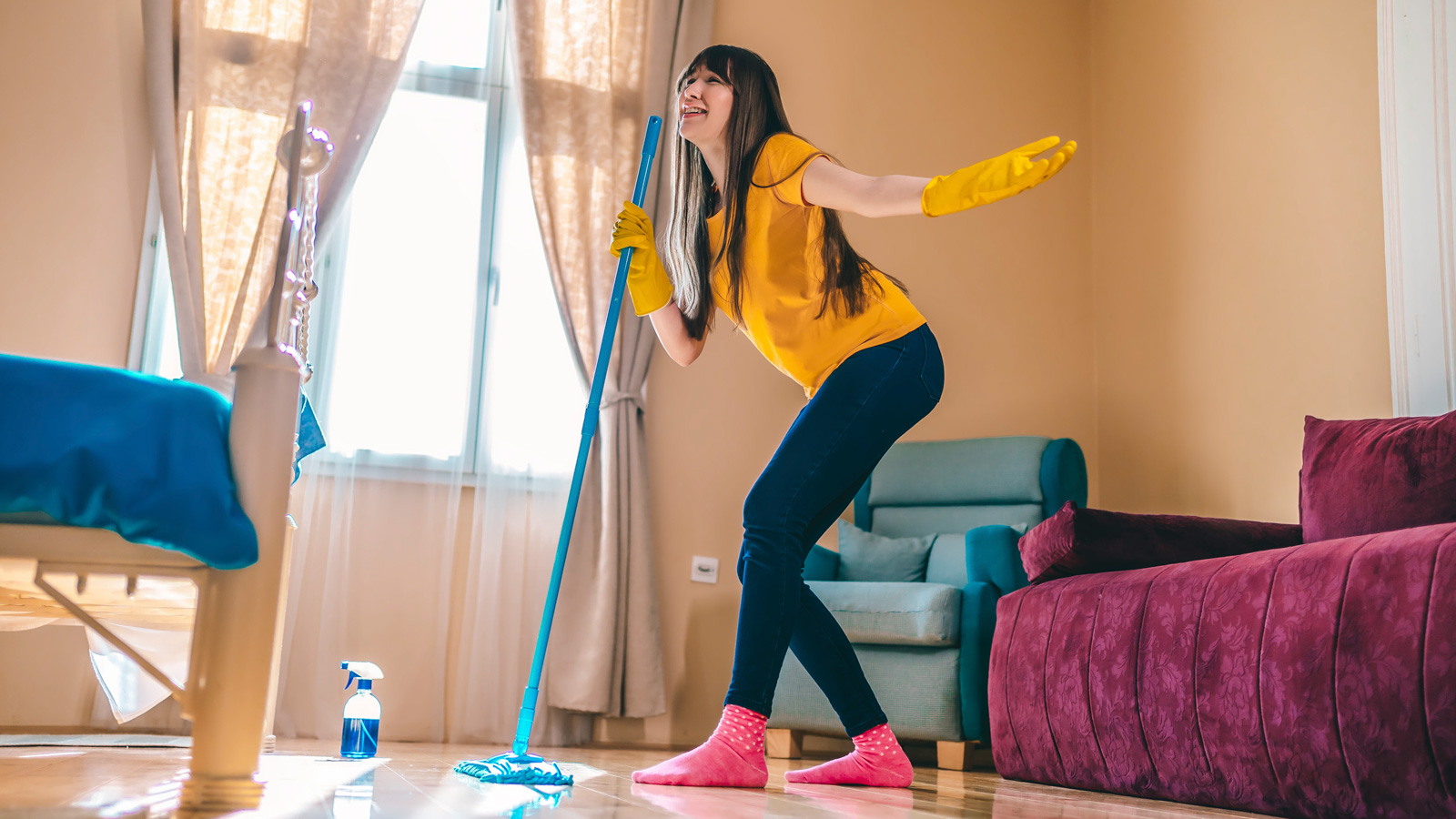 Happy woman cleaning home and having fun by singing at mop like on microphone