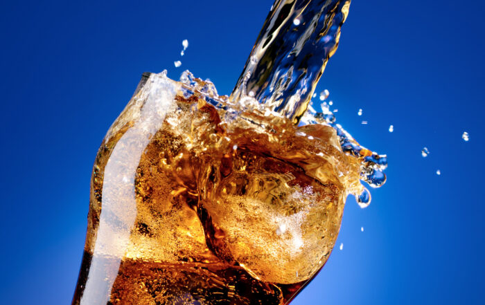 Glass of cola with a large pouring splash, isolated on blue
