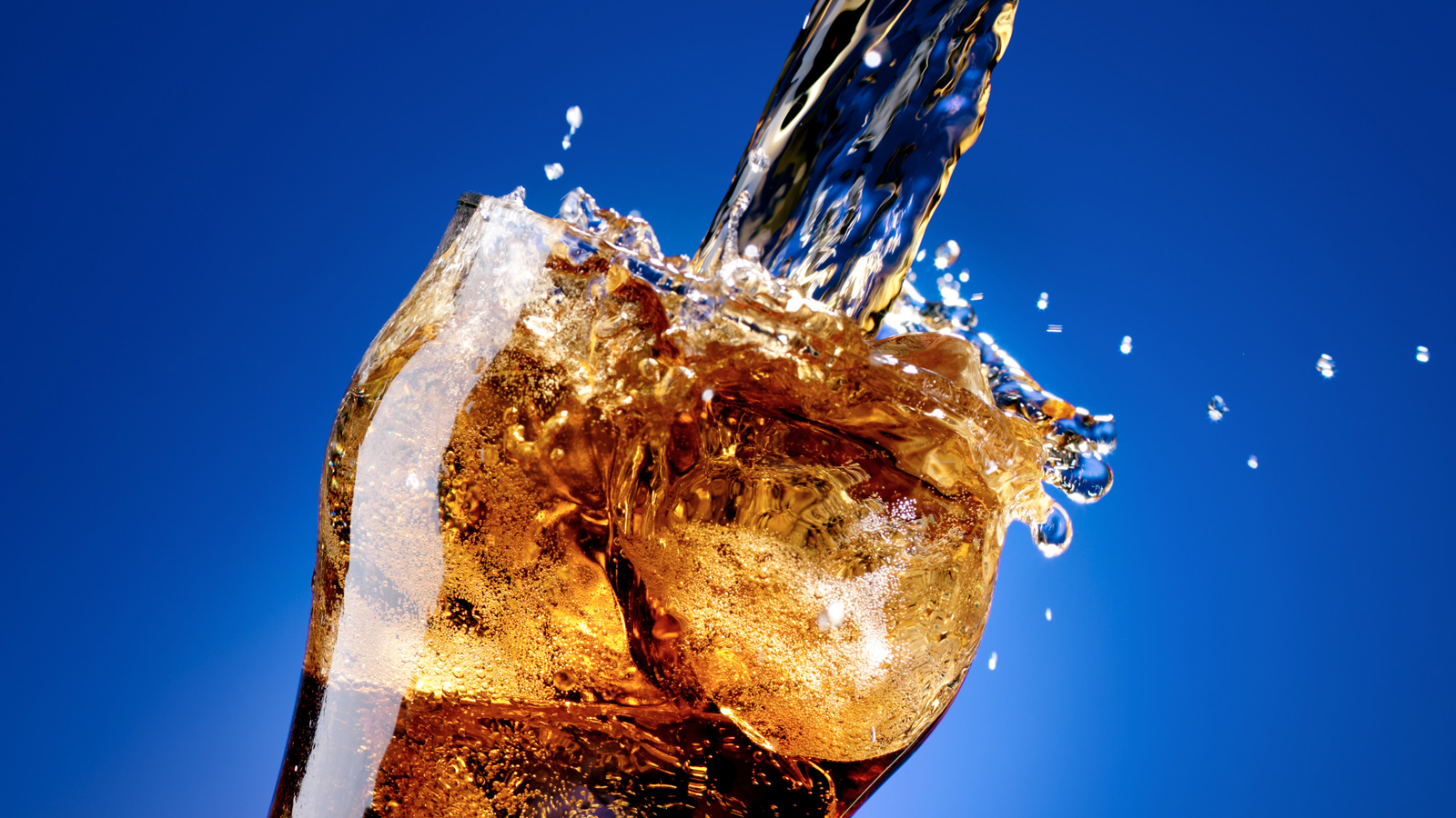 Glass of cola with a large pouring splash, isolated on blue