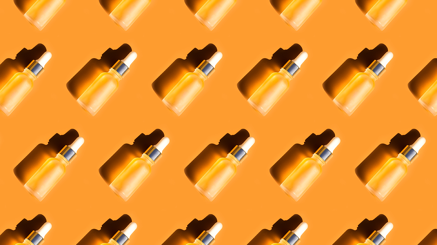 Trendy Skin care Pattern made with bottles with Beauty Product Facial Serum or Essential Oil on orange color background. Flat lay, Close-up.