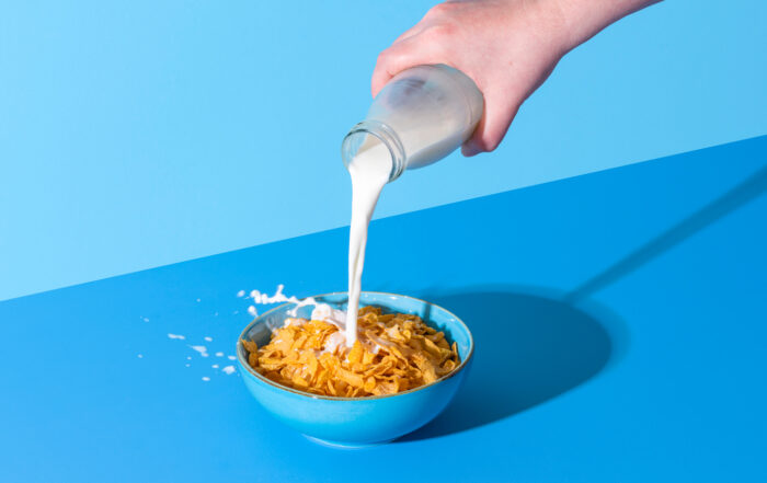 Pouring milk in a cereal bowl on a blue background. Cornflakes and milk.