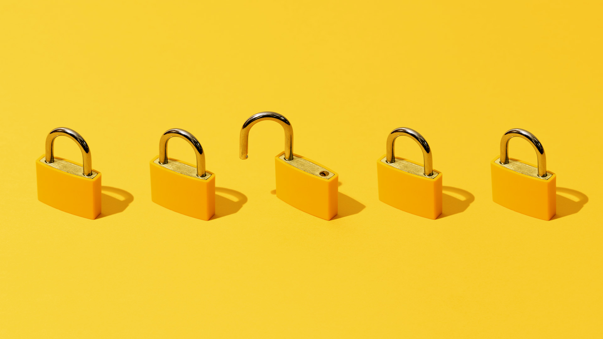 High angle view of five yellow padlocks on yellow background. One of them is open.