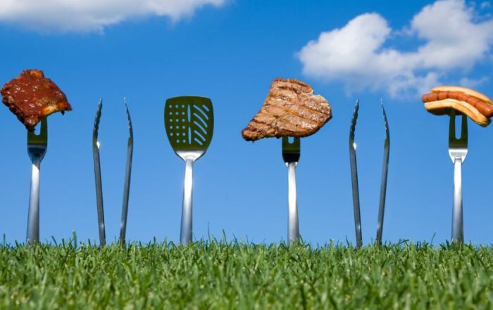 Grilling utensils stuck in the ground holding various grilled foods