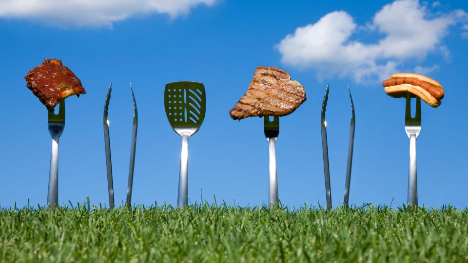 Grilling utensils stuck in the ground holding various grilled foods