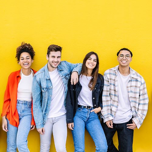 A group of happy young people posing in front of a yellow wall