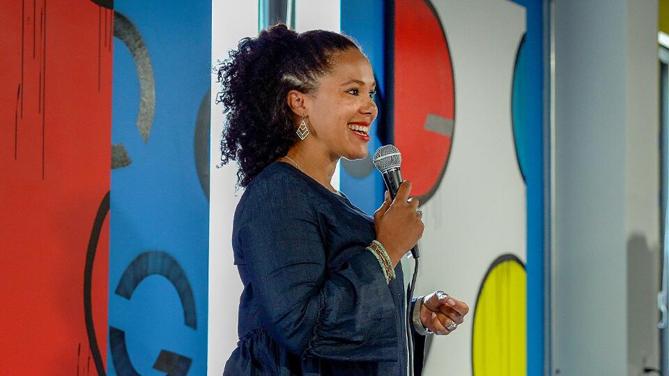 A woman speaking in front of a Quad MKE mural.
