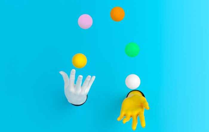 White and yellow hands juggling five colored balls in front of a light blue background