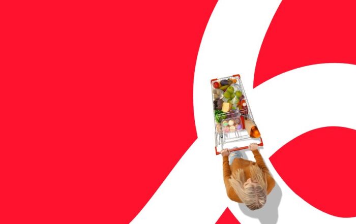 Consumer pushing a shopping cart filled with groceries while walking on a red and white path.