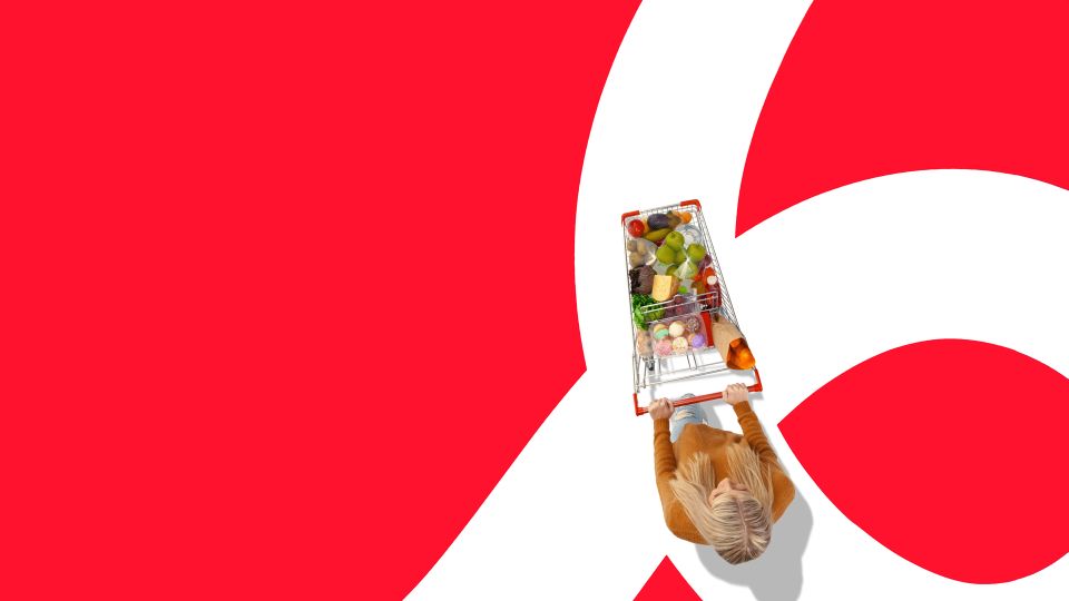 Consumer pushing a shopping cart filled with groceries while walking on a red and white path.