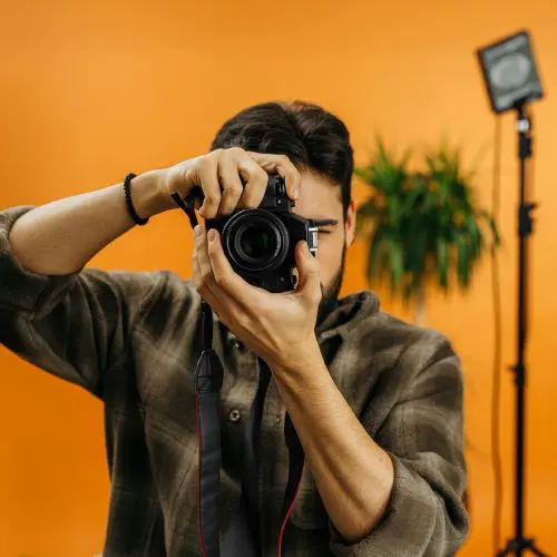A photographer in his orange painted studio taking a photo of the user - breaking the third wall