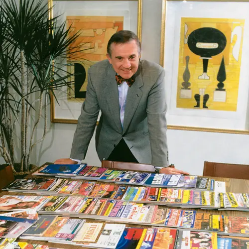 Harry Quadracci standing behind a table filled with a display of magazines printed by Quad