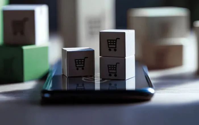 Three small boxes with a shopping cart icon design sitting on top of a cell phone