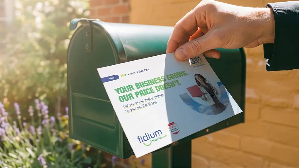A hand holding a Fidium postcard mailer A hand holding a Fidium postcard mailer